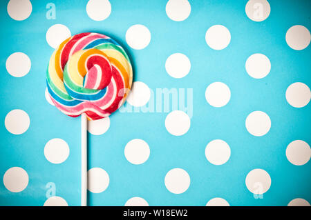 colourful sweet rainbow swirl lollipops on a blue polka dot background Stock Photo