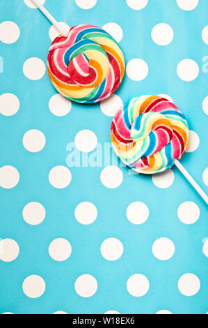 colourful sweet rainbow swirl lollipops on a blue polka dot background Stock Photo