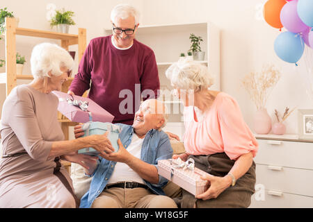 Two senior couples making gifts to each other while enjoying home party Stock Photo