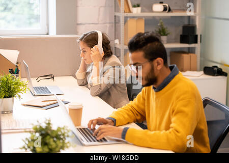 Serious busy multi-ethnic managers sitting at one table and using modern laptops while working with files in office Stock Photo
