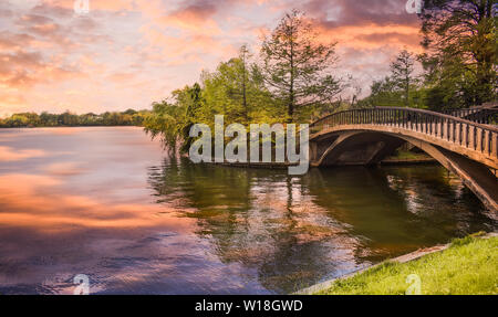 Footbridge over the pond in the city park at sunset. Styled stock photo with wooden bridge in twilight atmosphere in Herastrau Park from Bucharest. Ro Stock Photo