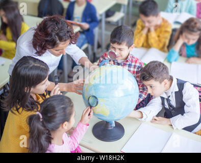 teacher and a group of students examines world map in lecture with magnifying glass Stock Photo