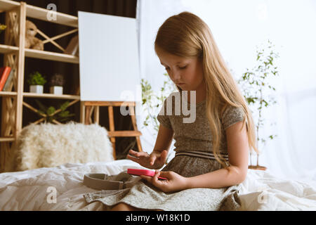 Girl using different gadgets at home. Little model sitting in her room with smartphone and gaming or using videochat with her friends. Concept of interaction of kids and modern technologies.