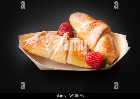 Homemade croissants in a bio wooden dish, isolated on black background. Two croissants and two strawberries on black Stock Photo