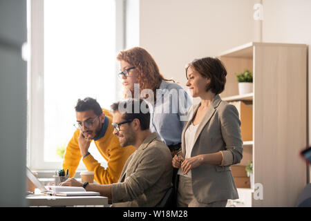 Pensive business team looking at laptop screen while viewing maquette of project with content web designer in modern office Stock Photo