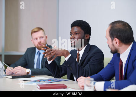 Young confident African-american delegate or trader explaining idea or making report at business seminar Stock Photo
