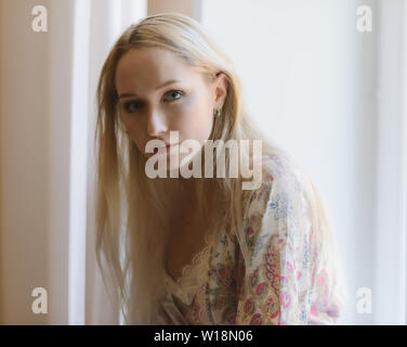 Pensive woman in bathrobe sitting on the windowsill. Natural light. Stock Photo