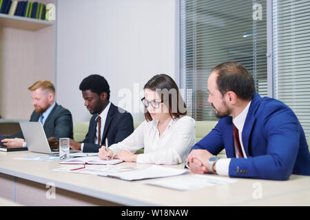 Team of young intercultural colleagues preparing their work while sitting in row Stock Photo