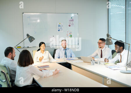 Group of young multicultural colleagues sitting in boardroom late in the evening and discussing new ideas Stock Photo