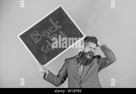 Teacher with tousled hair stressful about school year beginning. Teacher bearded man holds blackboard with inscription back to school green background. Keep working. Teaching stressful occupation. Stock Photo