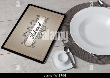 Tablet with stylish restaurant logo and laid table  Stock Photo