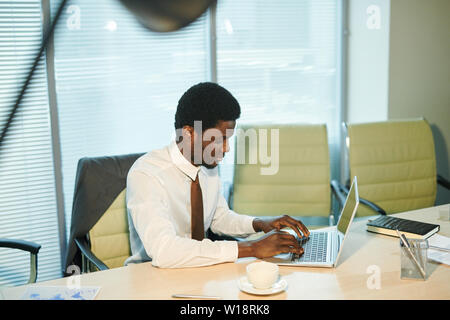 Serious young businessman planning work while sitting by desk, typing and looking at laptop display Stock Photo