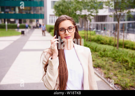 Close-up shot of businesswoman using a mobile phone and talking with somebody while walking on the street. Stock Photo