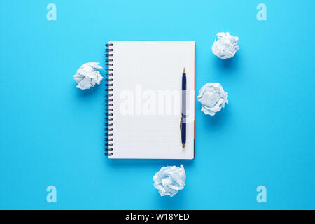 Open empty notebook, pen and crumpled paper balls on blue background. Creation process or creative attempts concept. Copy space. Stock Photo