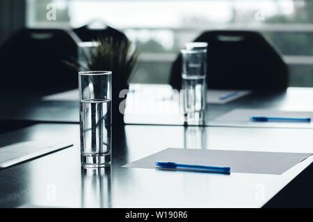 Close up of dark conference table water glasses pens, paper sheets Stock Photo