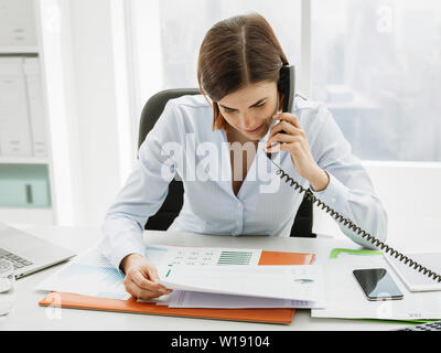 Corporate business executive sitting at office desk and working, she is making phone calls and checking financial reports Stock Photo