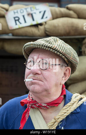 Kidderminster, UK. 29th June, 2019. Severn Valley Railways 'Step back to the 1940s' gets off to a fabulous start this weekend with costumed re-enactors playing their part in providing an authentic recreation of wartime Britain. A portrait, front view, close up of a man dressed as vintage ARP warden stands by air raid shelter comically called 'Hotel Ritz'. Character portraiture: man in tweed flat cap with cigarette in mouth. Credit: Lee Hudson Stock Photo