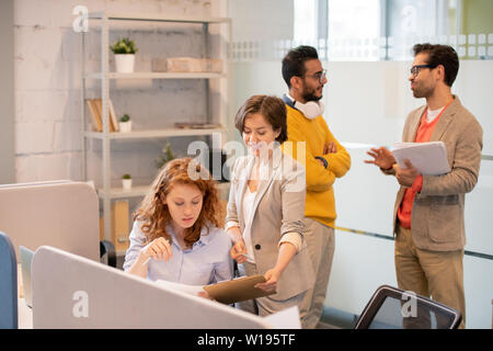 Creative employees working with data in office: product manager offering sales plan to colleague while men discussing paperwork in background Stock Photo