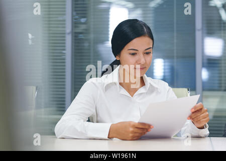 Pretty young brunette businesswoman reading financial document in office Stock Photo