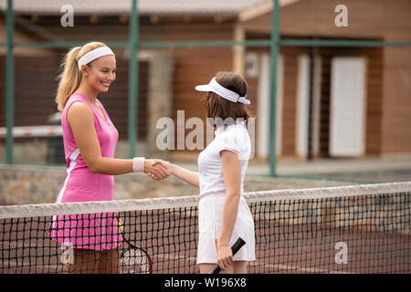 Two young female tennis players shaking hands over net before game on stadium Stock Photo