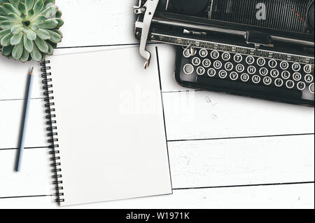 top view of vintage typewriter, blank notepad and pencil and succulent plant on rustic white wooden desk Stock Photo