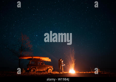 Happy couple man and woman standing in front burning bonfire Stock Photo