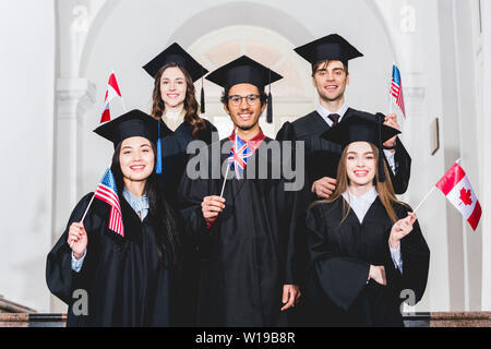 happy students in graduation gowns holding flags of different countries Stock Photo