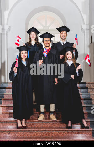 cheerful students in graduation gowns holding flags of different countries Stock Photo