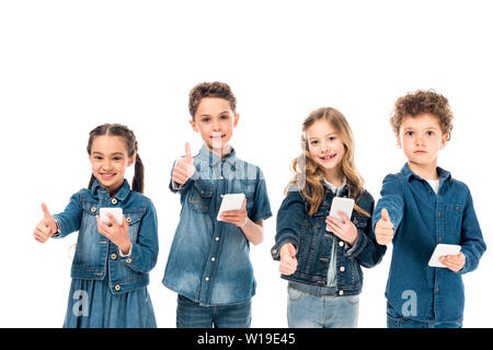 four kids in denim clothes using smartphones and showing thumbs up isolated on white Stock Photo