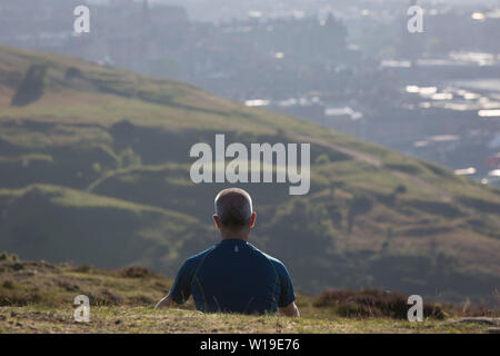 A man spends quiet, personal time overlooking the city of Edinburgh from Holyrood Park, on 26th June 2019, in Edinburgh, Scotland. Stock Photo