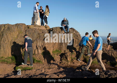 Walkers enjoy summer evening sunshine on the summit of Arthur's Seat in Holyrood Park, overlooking the city of Edinburgh, on 26th June 2019, in Edinburgh, Scotland. Arthur's Seat is an extinct volcano which is considered the main peak of the group of hills in Edinburgh, Scotland, which form most of Holyrood Park, described by Robert Louis Stevenson as 'a hill for magnitude, a mountain in virtue of its bold design'. The hill rises above the city to a height of 250.5 m (822 ft), providing excellent panoramic views of the city and beyond. Stock Photo