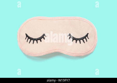 Pastel pink sleep mask with closed eyes embroidered on it with eyelashes on turquoise background. Top view, flat lay. Concept of vivid dreams. Accesso Stock Photo