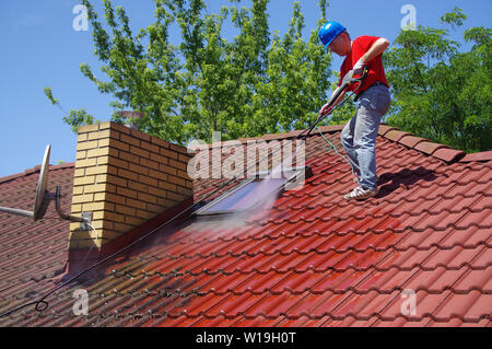House roof cleaning with pressure tool. Worker on top of building washing tile with professional equipment. Moss removing with water. Stock Photo