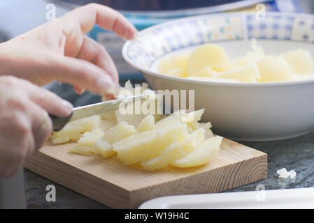 Hands holding a knife cutting some potatoes in a rustic kitchen. Empty copy space for Editor's text. Stock Photo