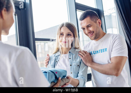 selective focus of attractive blonde woman taking clothes from multicultural volunteers Stock Photo