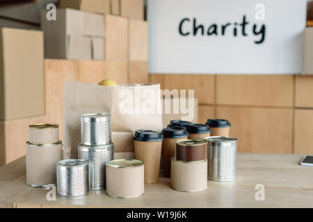 canned food, disposable cups and paper bag on wooden table in charity center Stock Photo