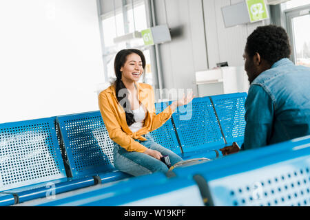 happy african american woman laughing while sitting in departure lounge with boyfriend Stock Photo