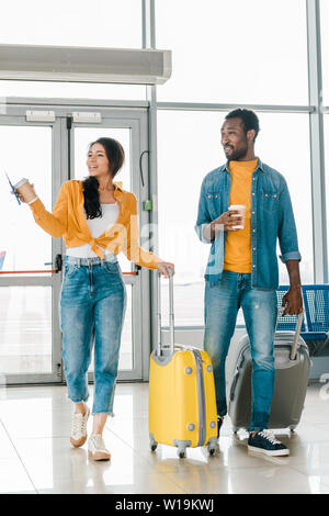 happy african american couple walking together in airport with travel bags and coffee to go Stock Photo Alamy