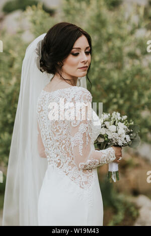 Bride holding wedding bouquet. Portrait of young bride wearing elegant lacey wedding gown. Stock Photo