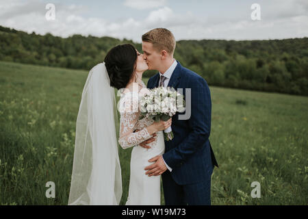 Bride and groom kissing on their wedding day. Just married couple in love sharing tender moments outside in nature. Stock Photo