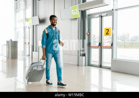 happy handsome african american man walking with suitcase in airport Stock Photo