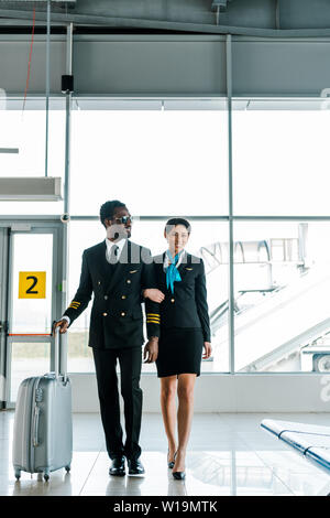 african american pilot and stewardess walking together in airport Stock Photo