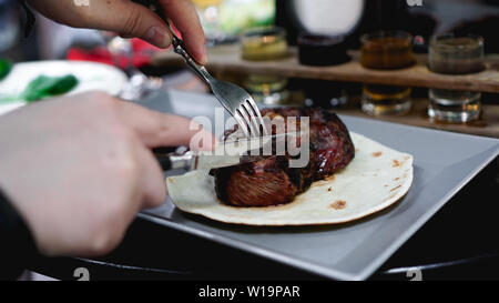 Mens hands cut juicy pieces of meat. He cuts steak on pita bread. Photos for the restaurant menu Stock Photo