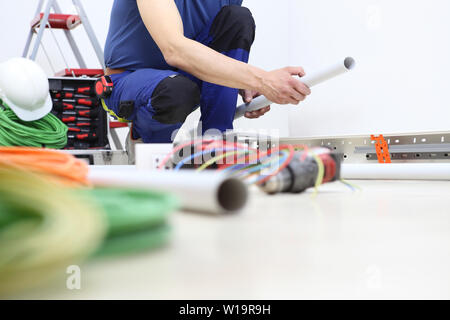 electrician at work with the plastic pipe in his hand to pass the electric cables to the sockets, electrical wiring Stock Photo