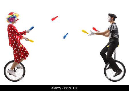 Full length profile shot of a mime and a clown on unicycles juggling with clubs isolated on white background Stock Photo