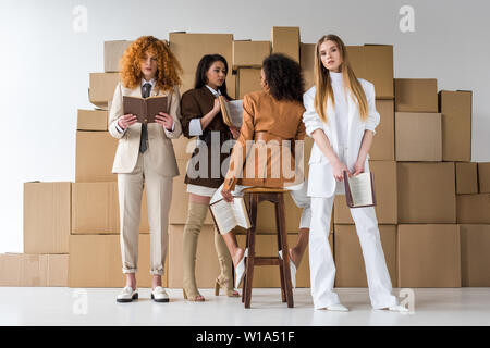 attractive multicultural girls holding books near boxes on white Stock Photo