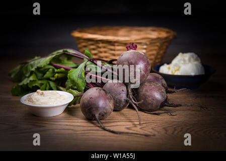 Bunch of raw beetroot on a wooden table with wicker basket and bowls of cream and horseradish Stock Photo