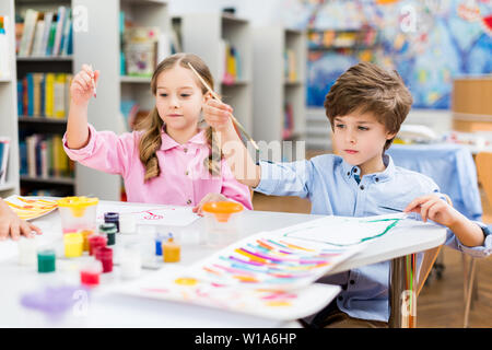 cute kids holding paintbrushes colorful gouache jars and papers Stock Photo