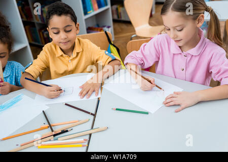 cute multicultural children drawing on papers with color pencils Stock Photo