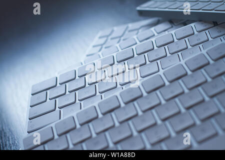 perspective view closeup of many white wireless aluminum computer keyboards on top of each other on a dark black wooden desk with natural light Stock Photo